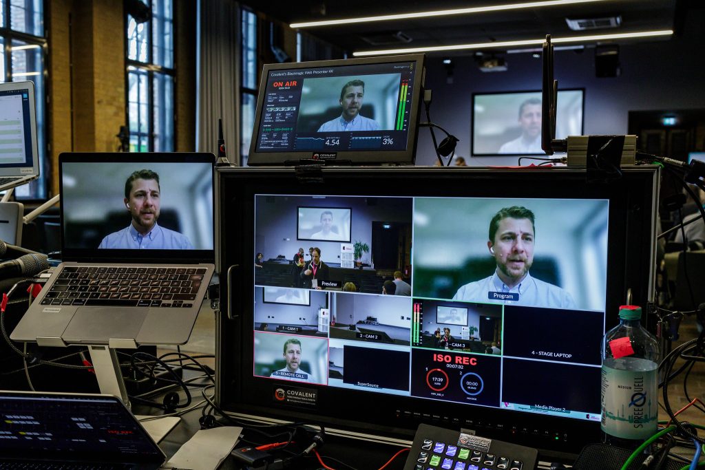 View from the event & recording technicians desk at FOSS Backstage. Four different monitors show the different camera angles.